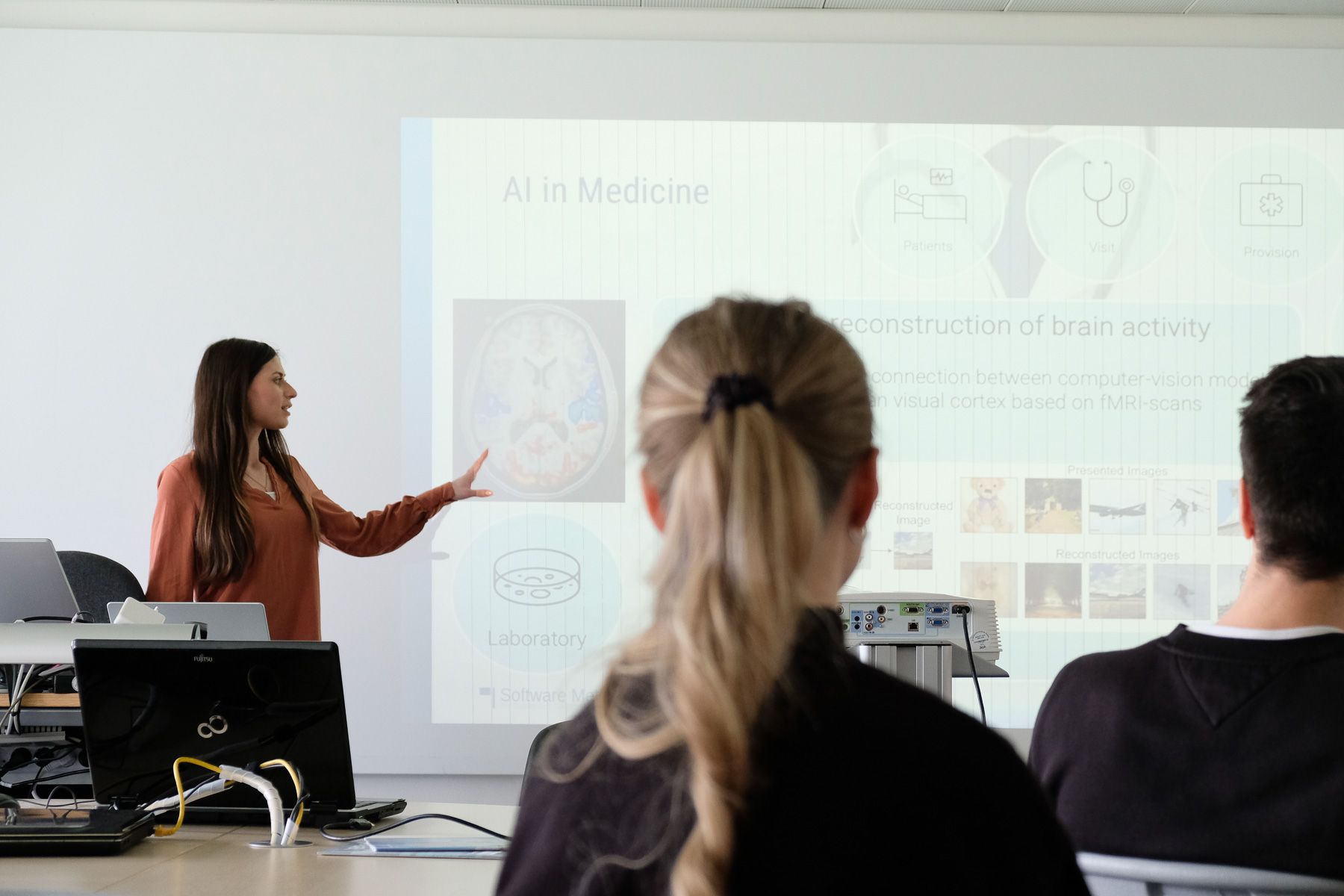 Miriam Elia presenting an AI in Medicine lecture, with slides showing brain activity reconstruction visible behind her